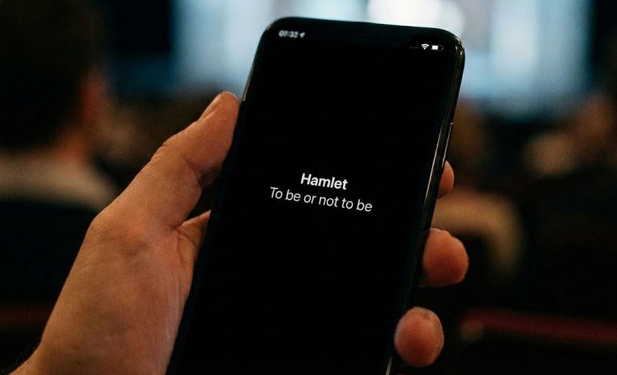 Ein Gast liest Theaterübertitel während einer Live-Vorstellung auf dem Smartphone