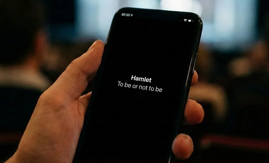 Audience member reading theatre surtitles on a phone during a live performance